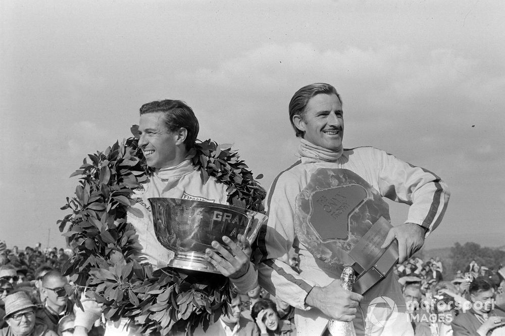 Jim Clark, 1st position, on the podium with his winners' trophy alongside teammate Graham Hill, 2nd position, with his pole position trophy